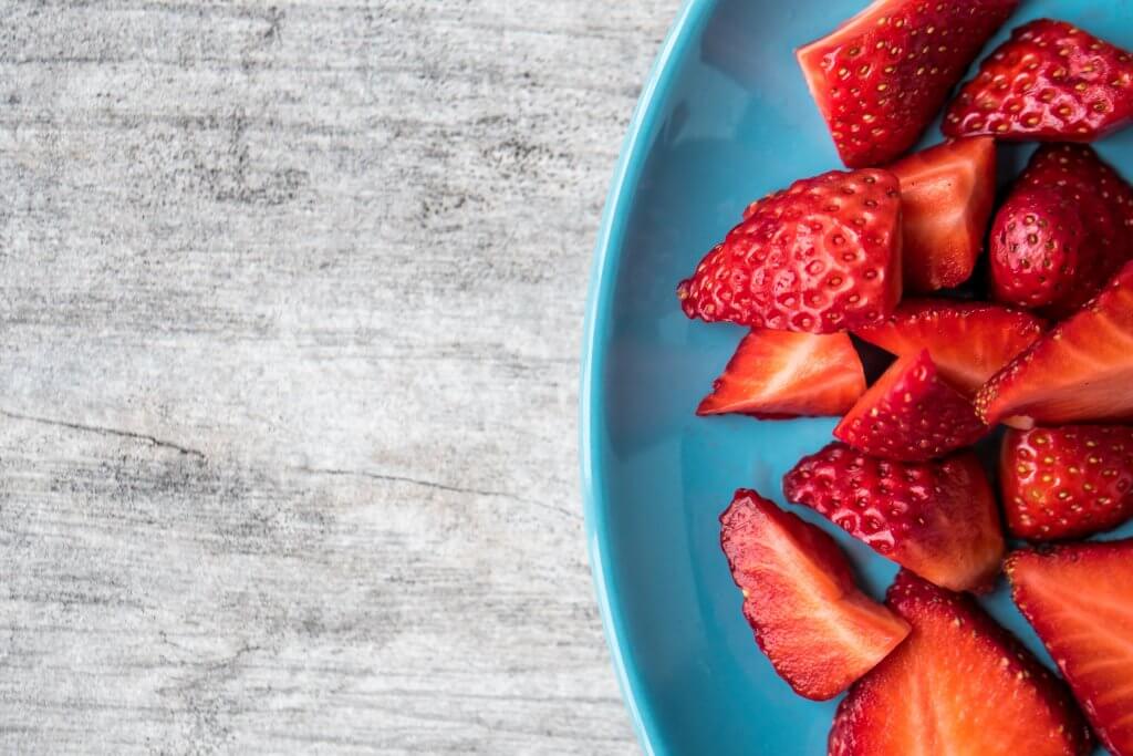 A white bowl filled with fresh, sliced strawberries.